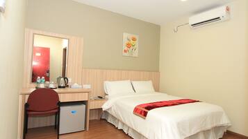 Habitación de hotel con cama, escritorio con silla, refrigerador pequeño, espejo y aire acondicionado.