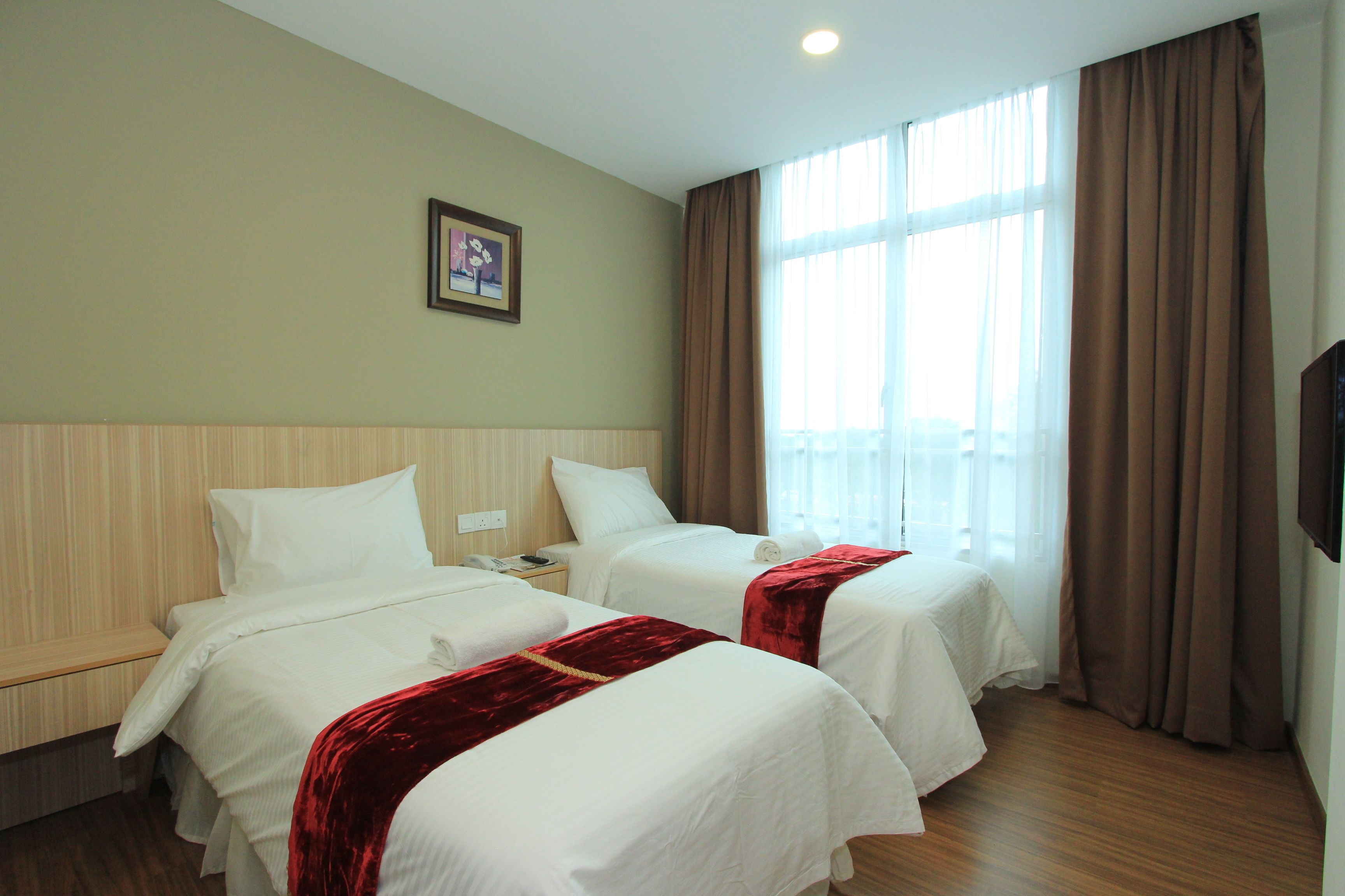 A hotel room with two beds, a wooden headboard, a window with curtains, and a framed picture on the wall.