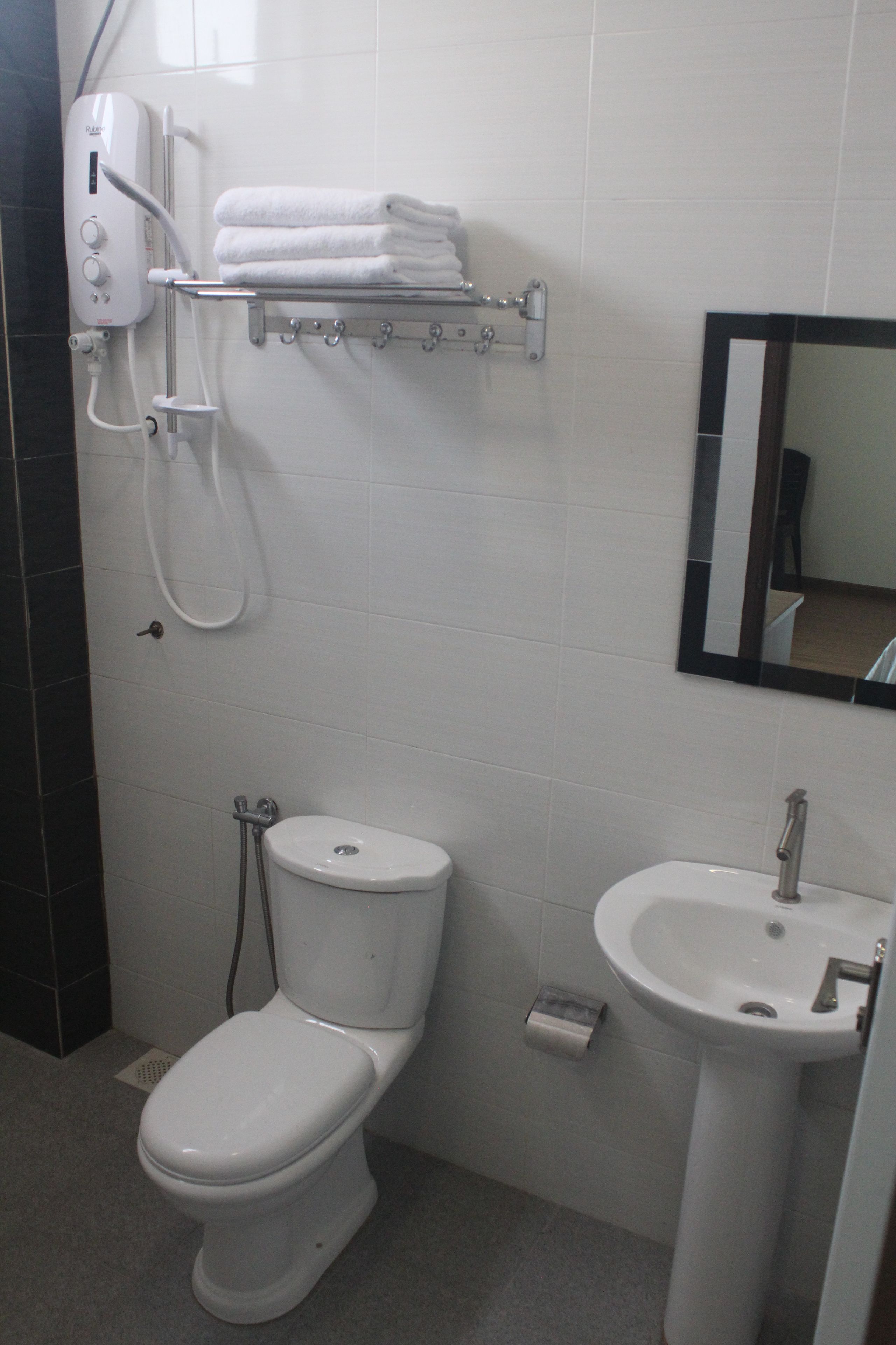 A bathroom with a toilet, a sink, a towel rack with towels, and a shower unit.
