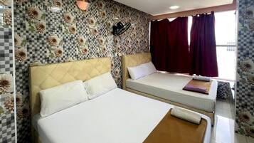 Habitación de hotel con dos camas, azulejos florales a cuadros en la pared, una ventana con cortinas rojas y una lámpara fijada a la pared.