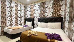 A hotel room with two beds, one with a black headboard and the other with a white headboard. There is a brown blanket on the larger bed and a purple towel on the smaller bed.