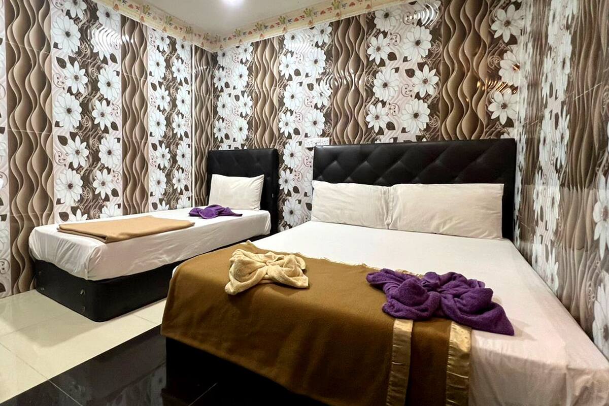 Camera d'albergo con due letti, uno con testiera nera e l'altro con testiera bianca. Sulla rete più grande c'è una coperta marrone e sul letto più piccolo un asciugamano viola.