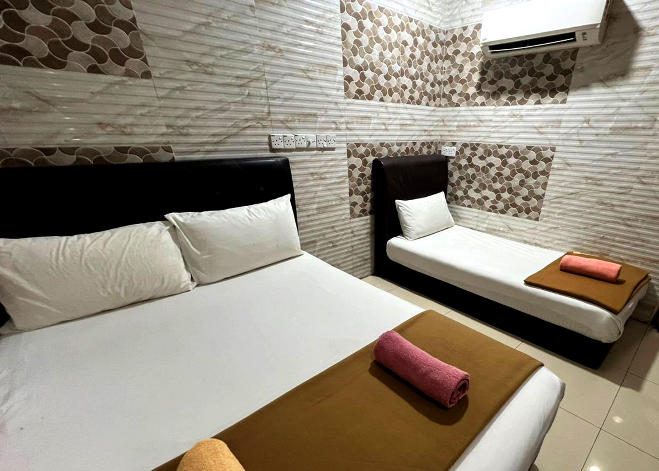 Habitación de hotel con una cama grande, una cama más pequeña y una cama sofá. Hay un aire acondicionado de pared y un enchufe en la pared.