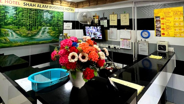 A hotel reception desk with a large floral arrangement, a digital screen, and a wall-mounted clock.