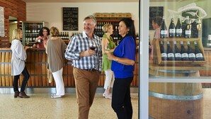 A group of people standing in a wine tasting area with a wooden counter and wine bottles displayed. - Vineyard Cottage at Upper Reach Winery (Baskerville)