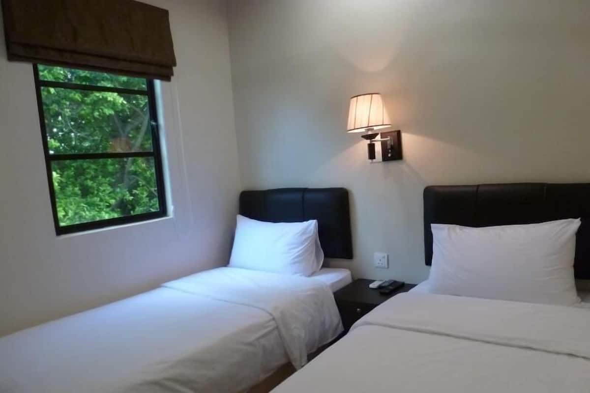 Ein Hotelzimmer mit zwei Einzelbetten, einem Nachttisch, einer Lampe und einem Fenster mit Blick auf Grünflächen.