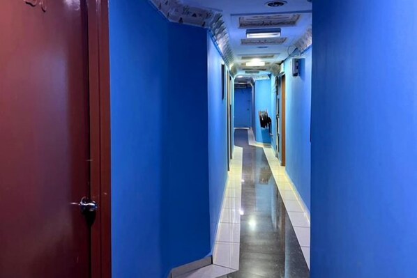 A corridor with blue walls and a red door, leading to a room with a bed and a window.