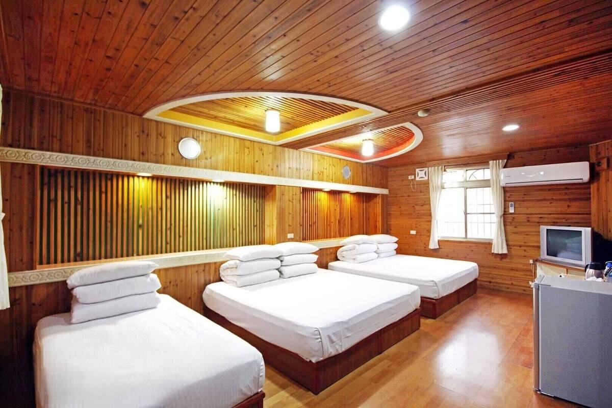 A wooden-paneled room with three beds, a television, and a desk.