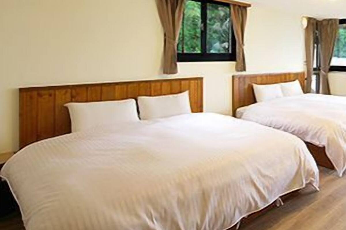 A room with two beds, wooden headboards, and a window with curtains.