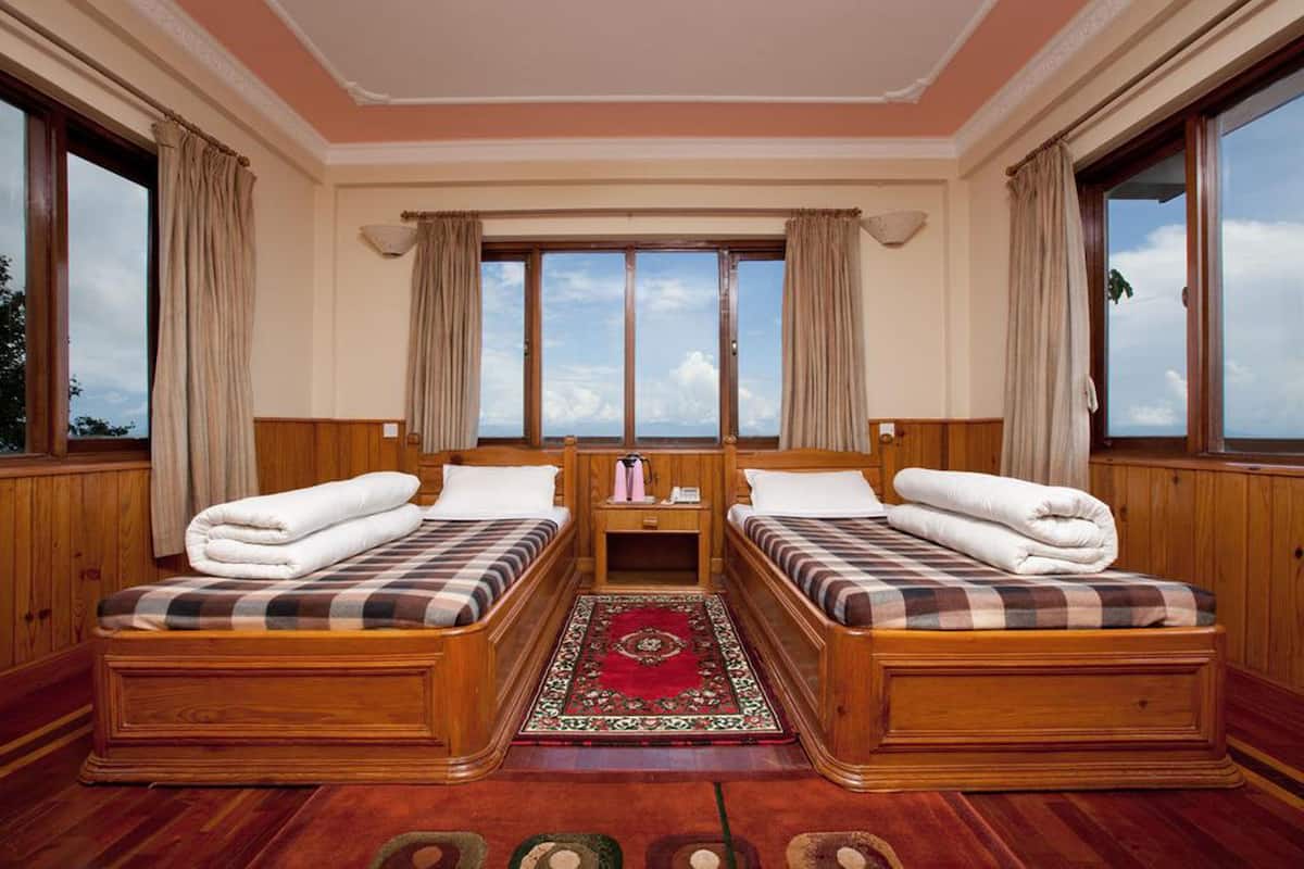 Une chambre avec deux lits en bois, une table de chevet placée au centre et une grande fenêtre avec des rideaux.