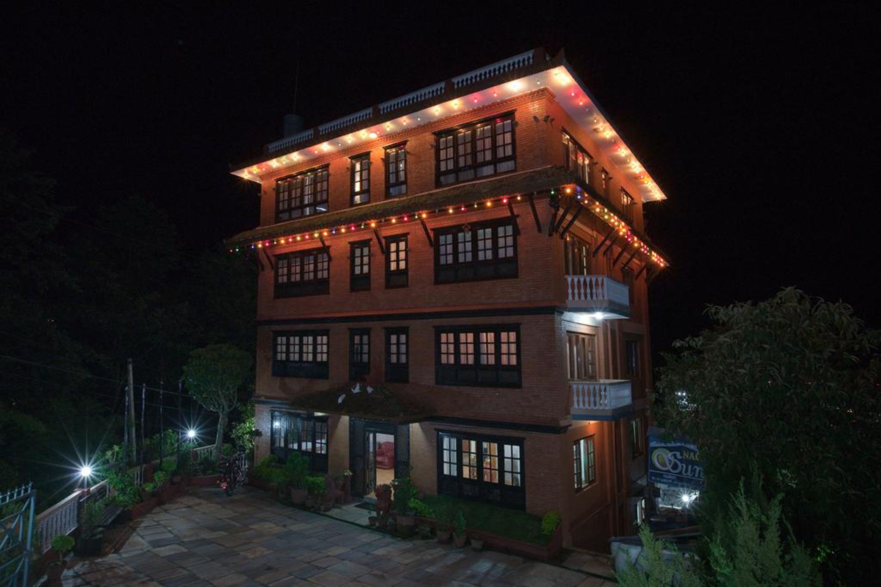 A two-story building with multiple windows and a balcony, surrounded by greenery.