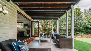 Une terrasse extérieure avec un canapé, une table basse en verre et un fauteuil en osier.