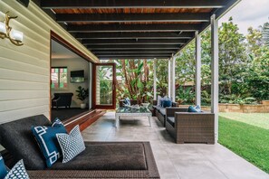 An outdoor patio with a sofa, a glass coffee table, and a wicker chair. - Balmoral Queenslander (Balmoral)