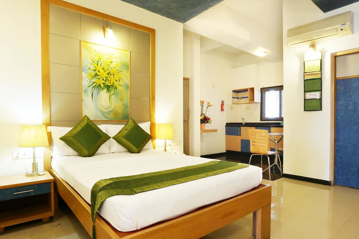 Una habitación de hotel con cama, mesitas de noche, escritorio y kitchenette.