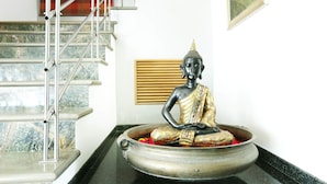 Une statue de Bouddha dans un récipient orné de fleurs, un escalier et une fenêtre donnant sur un paysage.