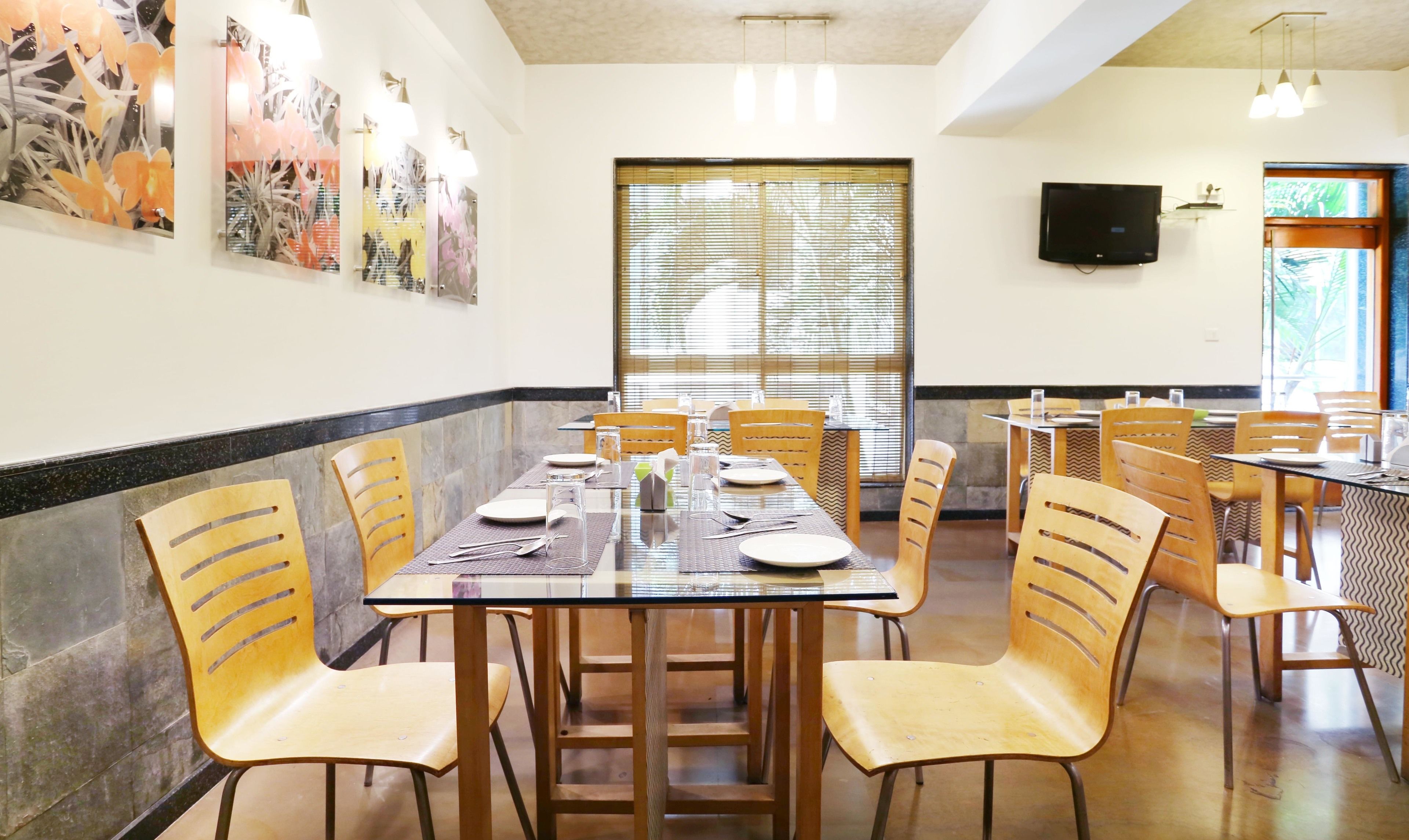 Un comedor con varias mesas y sillas, un ventanal con persianas y obras de arte colgadas en la pared.