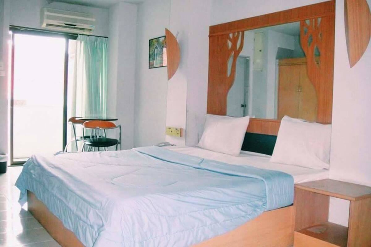 A hotel room with a bed, a wooden headboard, a chair, and a window with curtains.