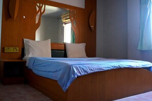Una cama individual con cabecera de madera y colcha azul. Hay una mesita de noche con una lámpara y un enchufe en la pared.