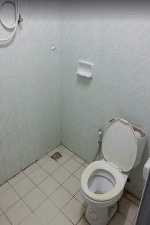 Un baño pequeño con azulejos, un inodoro, un secamanos y un cubo de basura.