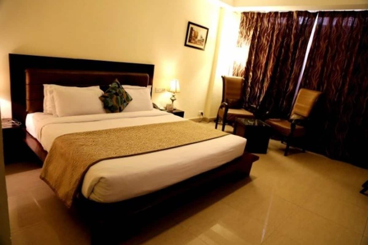 A hotel room with a large bed, a nightstand, a chair, and a curtain.