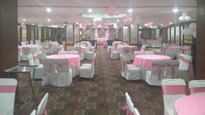 A banquet hall with round tables covered in pink tablecloths, white chairs with pink sashes, and a carpeted floor.