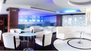 A modern hotel lobby with round tables, white sofas, and a blue-lit wall.