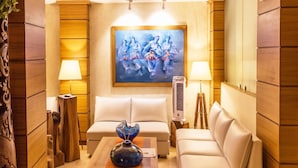 A modern living room with a white sofa, a coffee table with a blue vase, and two floor lamps. A painting is on the wall above the sofa. - Sangai Continental The Boutique Hotel (Imphal)