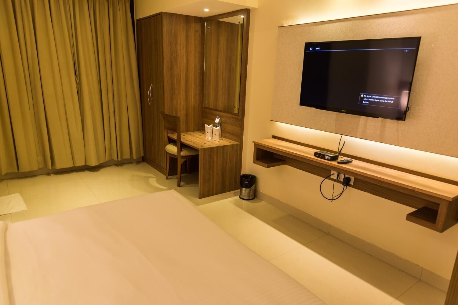 Ein Hotelzimmer mit Bett, einem an der Wand befestigten Fernseher, einem Holztisch und einer kleinen Sitzecke.