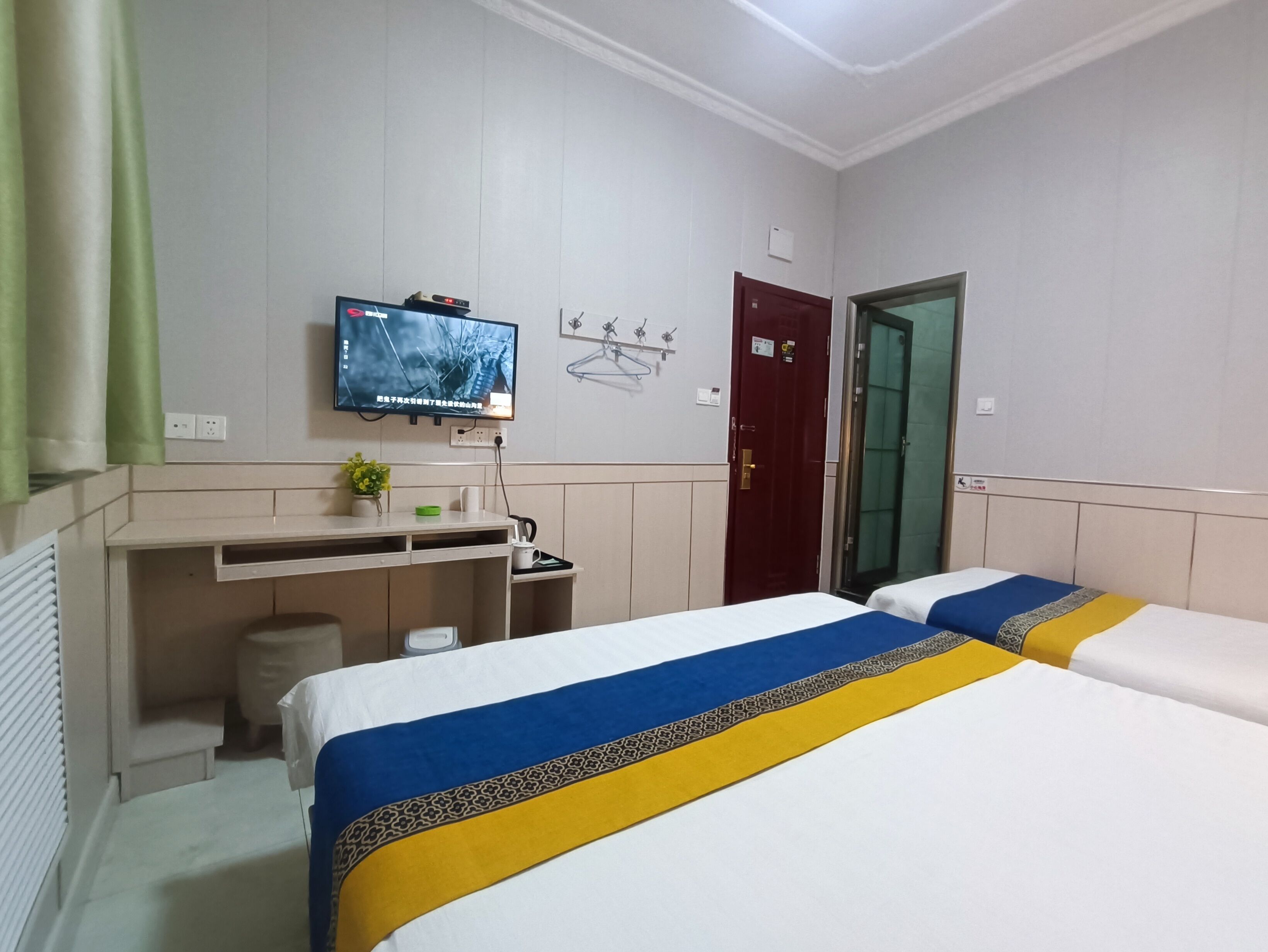 A hotel room with a bed, a desk, a television, and a door.