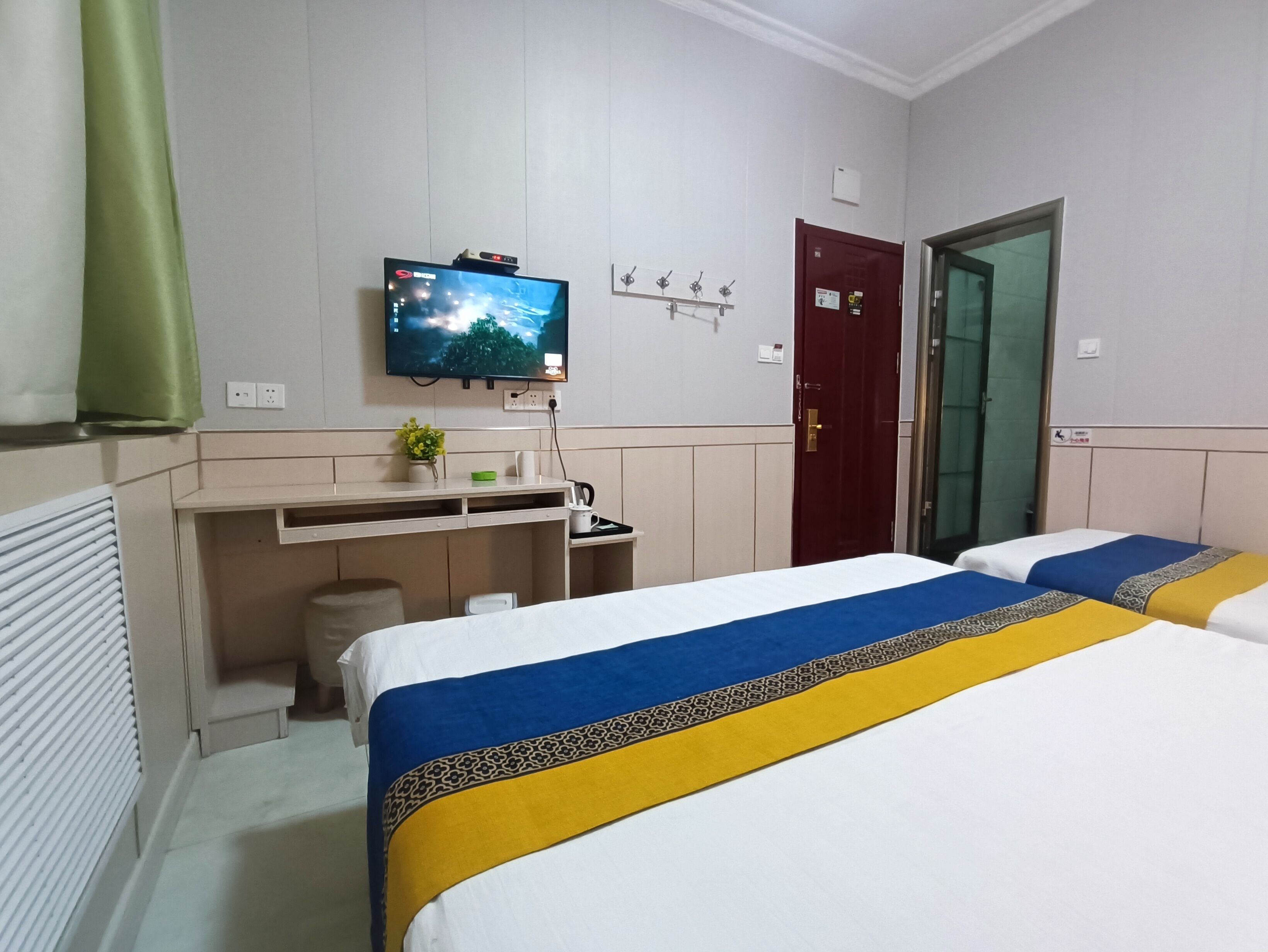 A hotel room with a bed, a desk with a computer, a television, and a door.