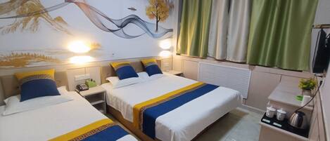 A hotel room with two beds, a mural on the wall, a kitchenette, and green curtains.