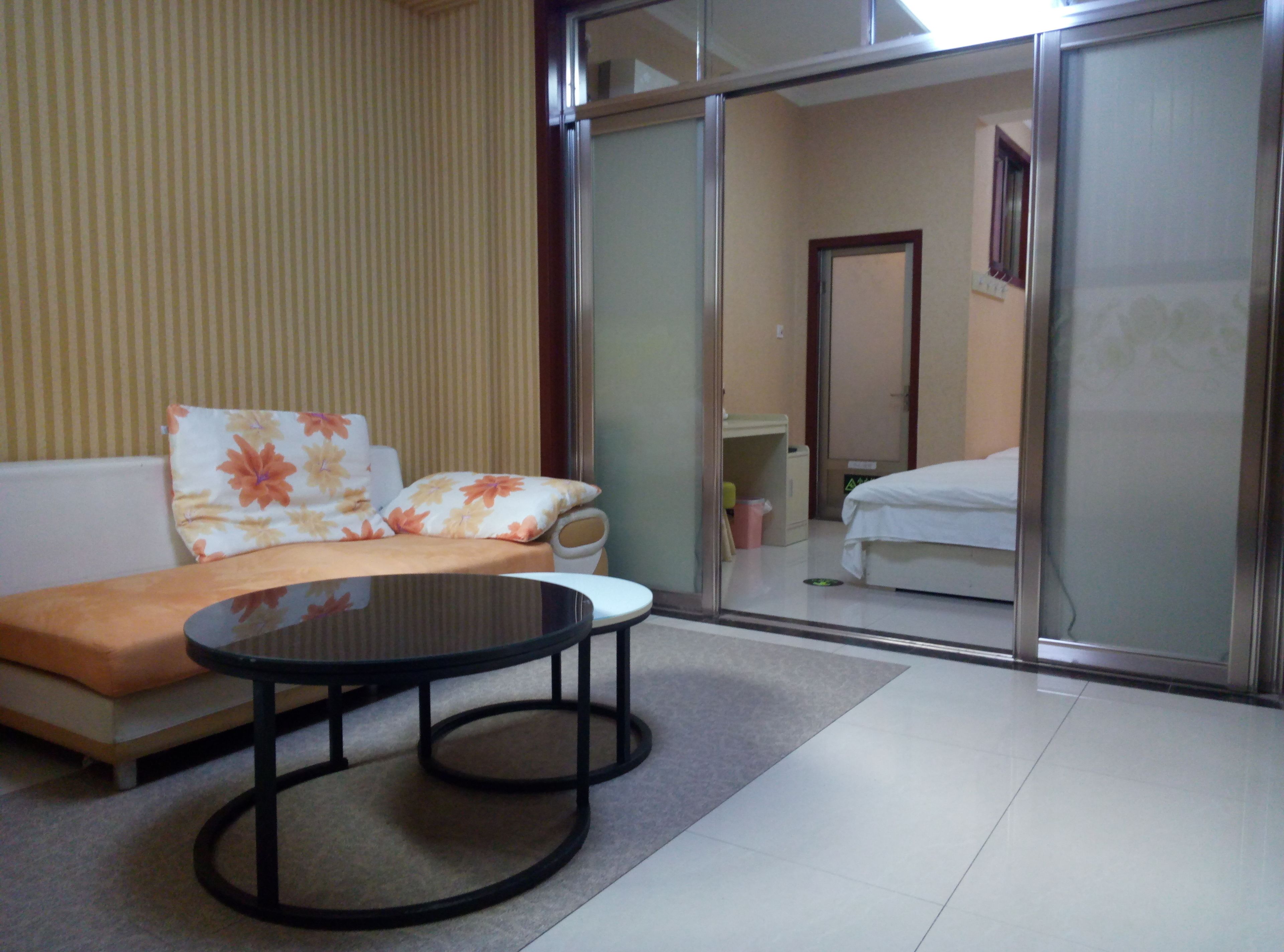 A hotel room with a sofa, a small round table, a bed, and a sliding door leading to a bathroom.