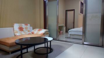 A hotel room with a sofa, a small round table, a bed, and a sliding door leading to a bathroom.
