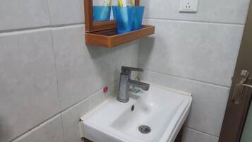 Un baño con un lavabo blanco, un espejo y una repisa de madera sobre el espejo con tazas azules.