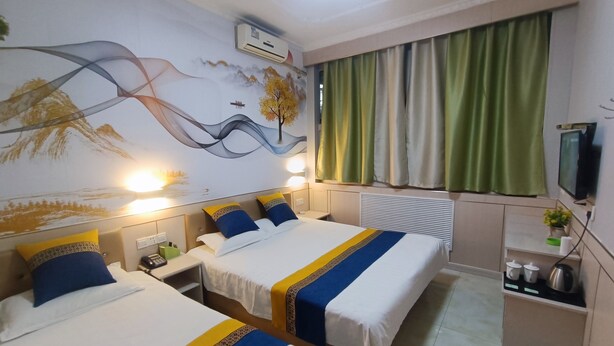 Una habitación de hotel con dos camas, un mural en la pared, un equipo de aire acondicionado, un televisor y una kitchenette pequeña.