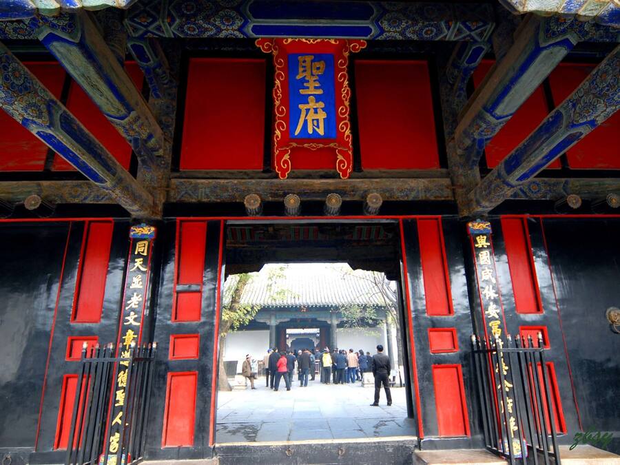 A traditional Chinese gate with intricate blue and red decorations, leading to a courtyard with a group of people.
