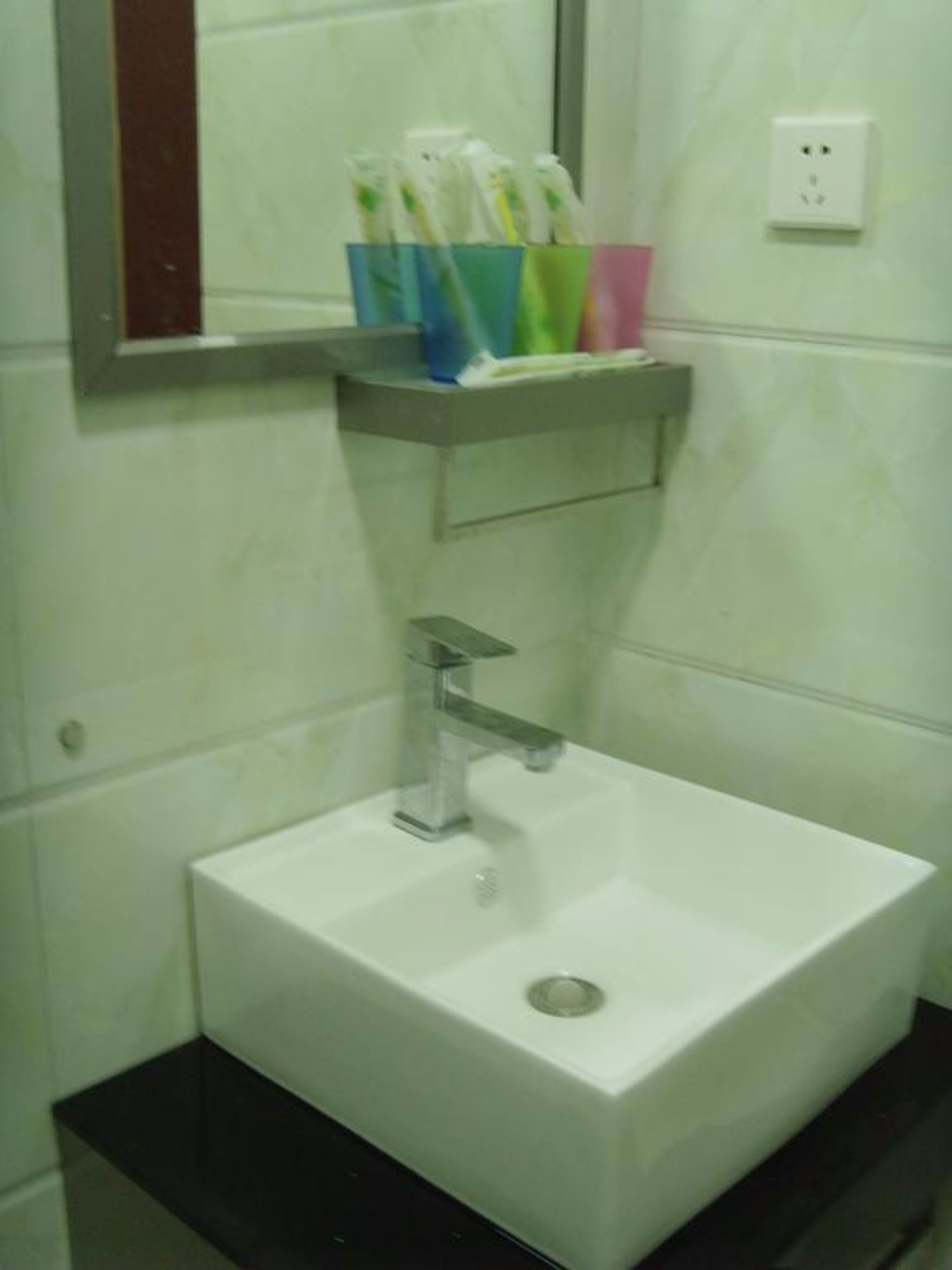 Un baño con un lavamanos blanco, un espejo encima y un estante con cepillos de dientes.
