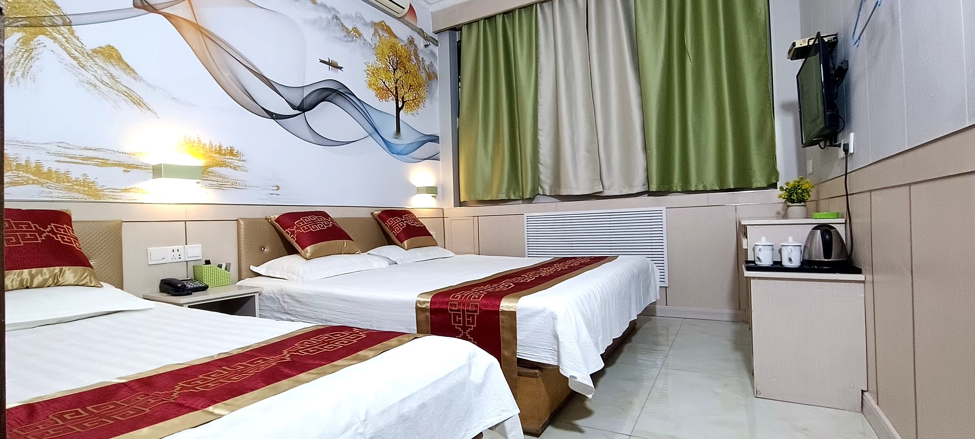 Habitación de hotel con dos camas, un escritorio, una kitchenette pequeña y un televisor montado en la pared.