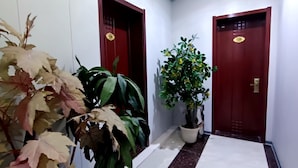 Un pasillo con dos puertas, cada una con un número. Hay plantas en macetas a ambos lados del pasillo.