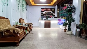 Zona de recepción con mostrador, área de descanso con dos sillas y una planta en maceta.