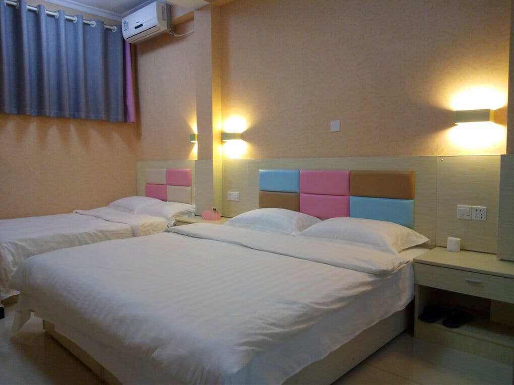 Habitación de hotel con dos camas, una mesita de noche, una lámpara y un aire acondicionado instalado en la pared.