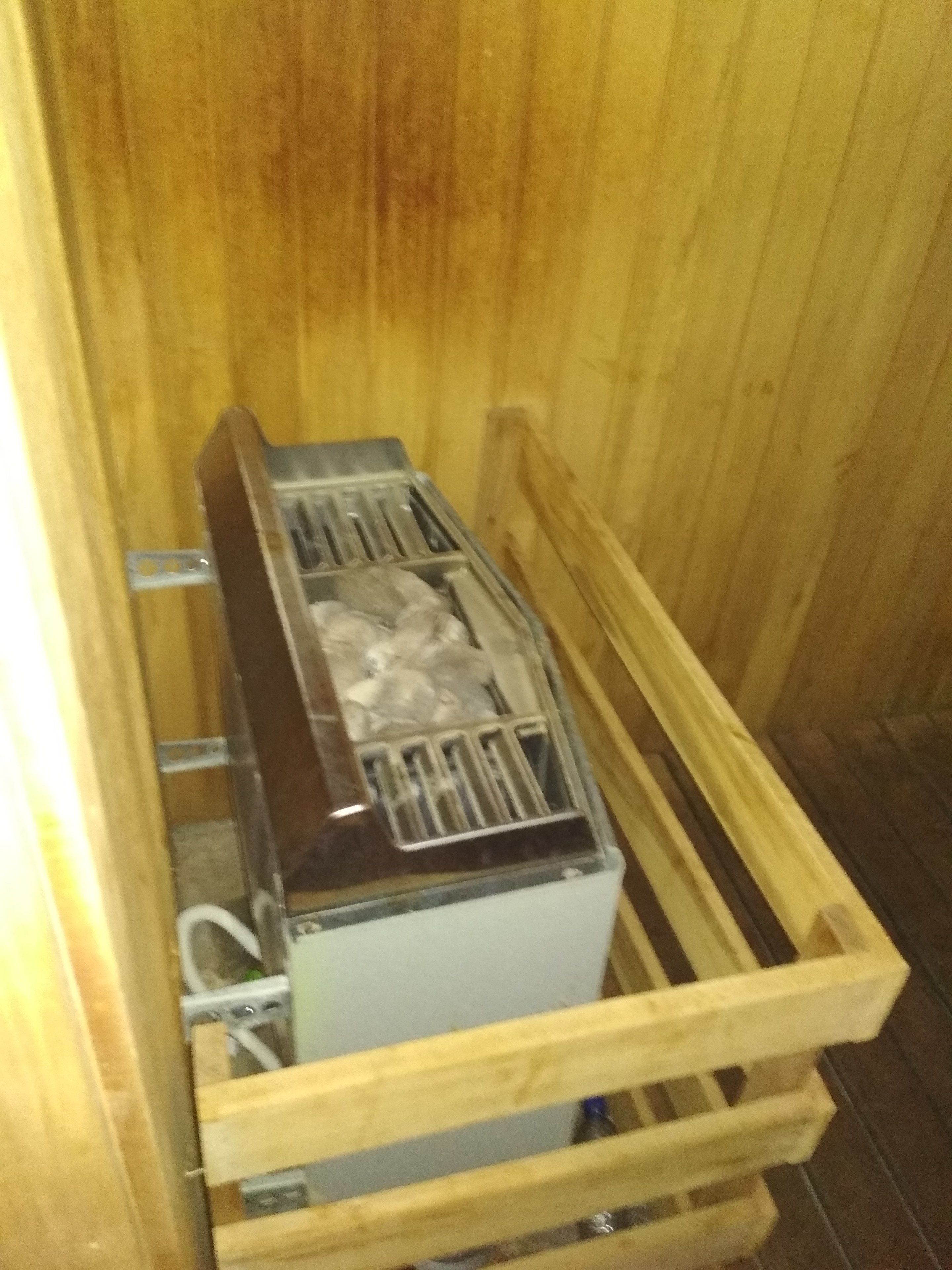 Een sauna met houten wanden, een metalen rooster en een wit bedieningspaneel.