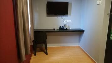 A room with a flat-screen TV mounted on the wall, a desk with a chair, and a tiled floor.