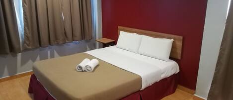 Ein Hotelzimmer mit Bett, Nachttisch, Fenster mit Vorhängen und einer roten Wand.