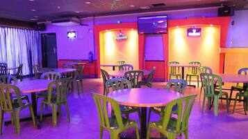 Un restaurante con varias mesas y sillas, un letrero de Heineken y una pantalla de televisión en la pared.