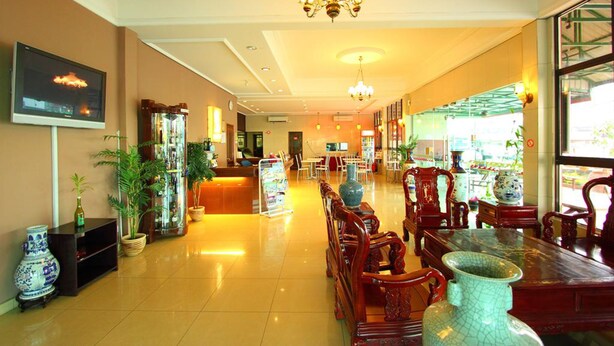A hotel lobby with a reception desk, seating area with wooden chairs, a chandelier, and a television on the wall. - Grandpa Hotel (Port Dickson)