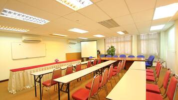 A conference room with long tables, red chairs, a whiteboard, and a projector screen.