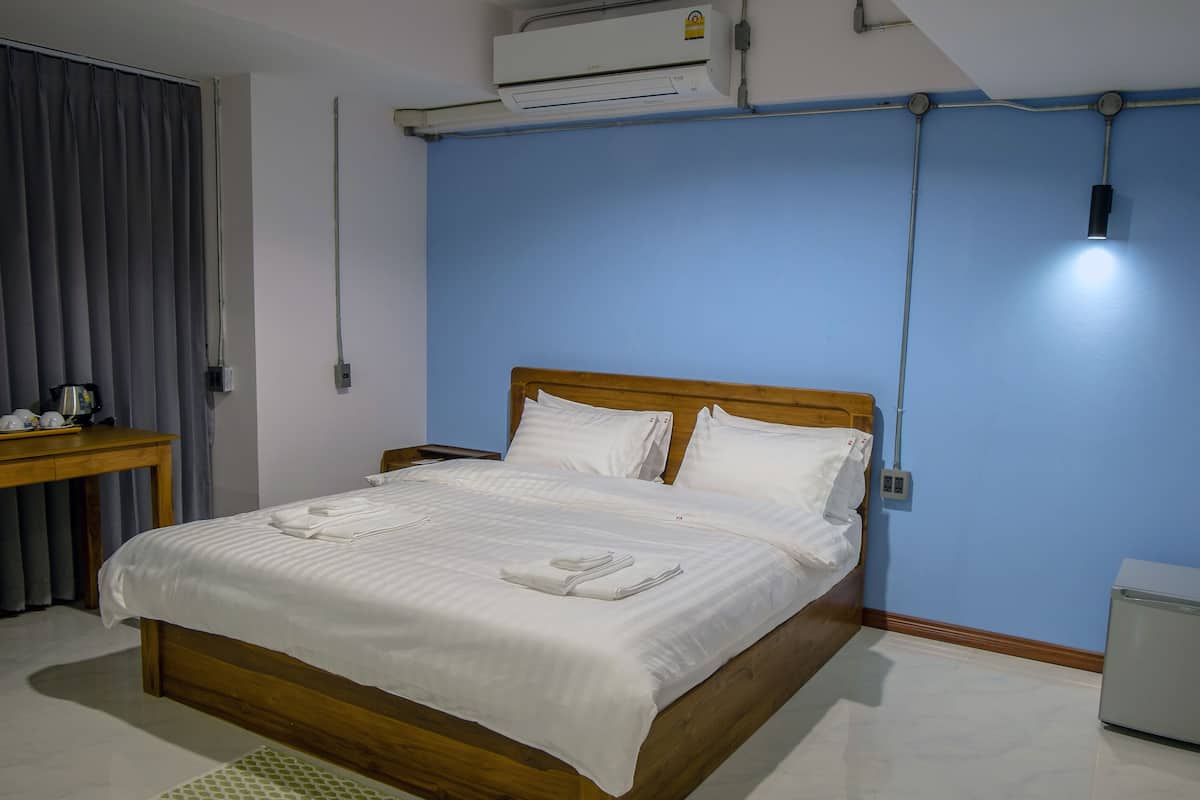 A neatly made bed with white linens, a wooden headboard, and a bedside table with a kettle and cups.