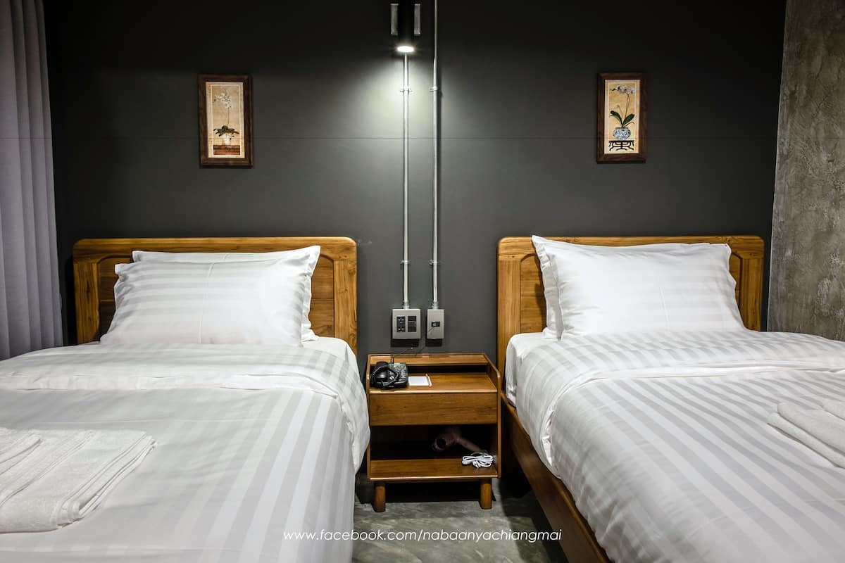 A hotel room with two beds, a nightstand with a lamp, and artwork on the walls.