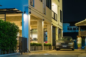 Um edifício moderno com um carro estacionado na frente, uma entrada com portão e uma pessoa passando.